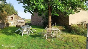Un cadre extérieur rustique avec un bâtiment en pierre, un arbre et du mobilier d’extérieur.