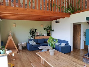 A living room with a blue sofa, a wooden coffee table, a wooden bench, a teepee, and various potted plants.