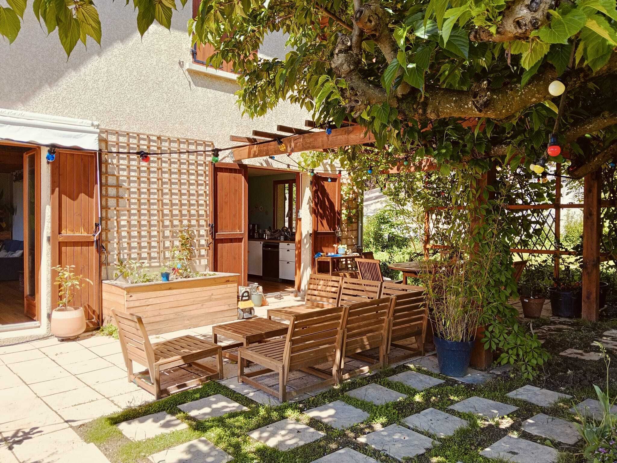 A patio with wooden furniture, a pergola, and potted plants.