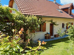 Ett hus med ett rött tegeltak, en trädgård med olika växter och en liten träbyggnad.