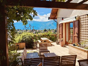 A patio with wooden furniture, potted plants, and a view of a mountainous landscape.