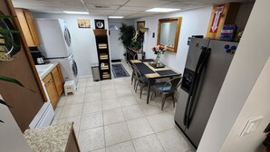 Eine kompakte Küche mit Kühlschrank, Spüle und einem Esstisch mit Stühlen. An der Wand ist ein Feuerlöscher angebracht und auf der Arbeitsfläche steht ein kleiner Topf mit Pflanze.