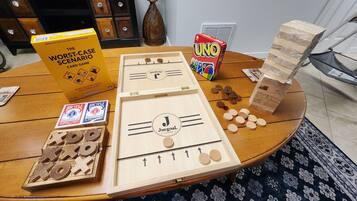 A wooden table with a board game, UNO cards, a book titled "The Worst-Case Scenario Card Game," and a UNO box.