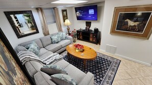 Ein Wohnzimmer mit grauem Sofa, einem Holztisch, einem Fernseher und einem gerahmten Bild von einem Hund.