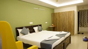 A hotel room with a large bed, a yellow chair, a wooden wardrobe, and a small table with a lamp. - hotel cozy (Hyderabad)