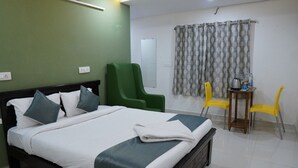 A hotel room with a bed, a green armchair, two yellow chairs, and a small table with a kettle and bottles. - hotel cozy (Hyderabad)
