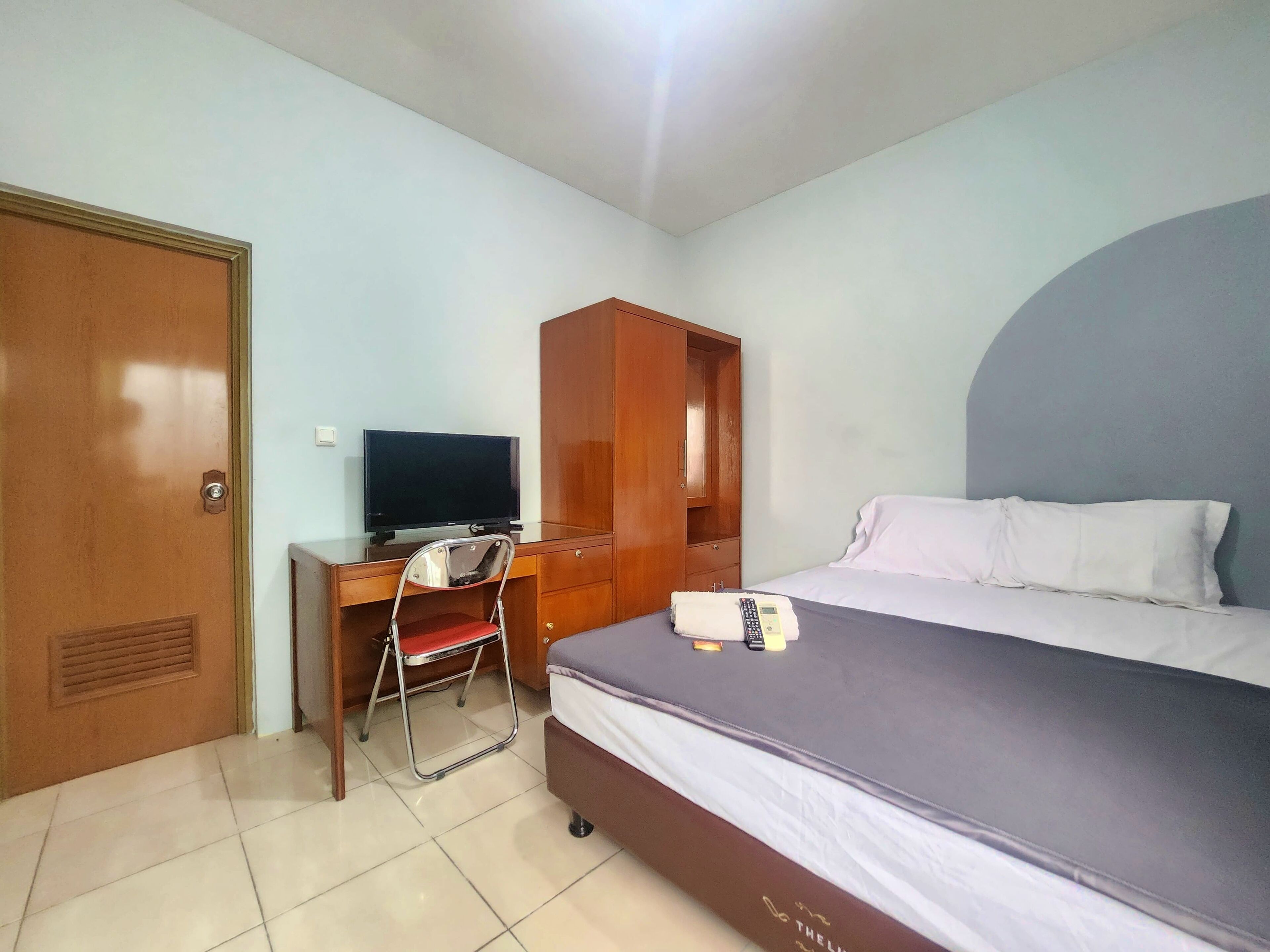 Una habitación de hotel con cama, escritorio con televisor, armario y una silla.