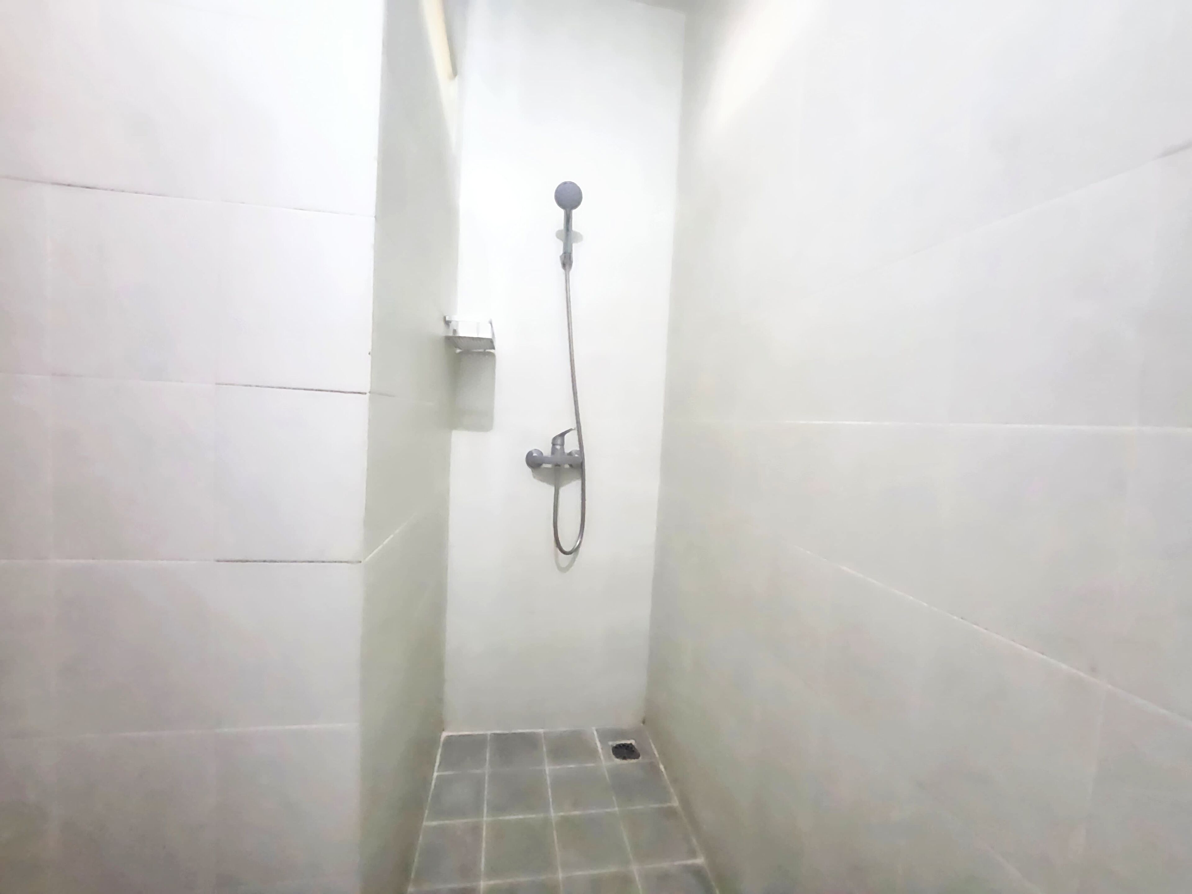 A small, tiled shower area with a handheld showerhead and a wall-mounted faucet.