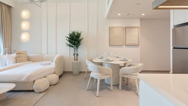 Una habitación de hotel moderna con cama, una mesa de comedor con sillas, una planta en maceta y una zona de cocina.