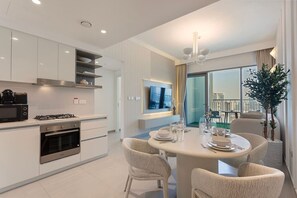A modern kitchen with white cabinetry, a gas stove, and a built-in oven. There is a dining area with a round table and four chairs, and a large window offering a view of the city.