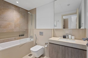 A modern bathroom with a bathtub, toilet, and vanity with a mirror. - Bright and Exquisite 1-Bedroom in Downtown views 2 (Dubai)