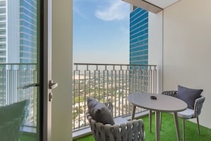 A balcony with a view of a cityscape, a round table, two chairs, and a small patch of artificial grass. - Bright and Exquisite 1-Bedroom in Downtown views 2 (Dubai)