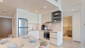 Una cocina moderna con armarios blancos, horno empotrado y estufa a gas. Hay una zona de comedor con una mesa redonda dispuesta para cuatro.