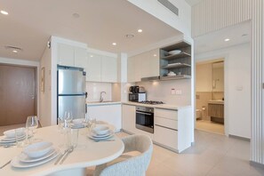 A modern kitchen with white cabinets, a built-in oven, and a gas stove. There is a dining area with a round table set for four. - Bright and Exquisite 1-Bedroom in Downtown views 2 (Dubai)