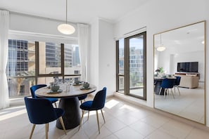 A modern dining area with a round table, blue chairs, and a large window offering a city view.
