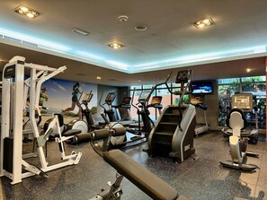 Ein Fitnessstudio mit unterschiedlichen Trainingsgeräten, darunter Laufbänder und Kraftgeräte, sowie ein großes Fenster mit Blick ins Freie.