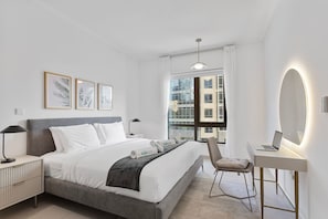 Ein modernes Hotelzimmer mit einem Bett, Nachttischen, einem Schreibtisch mit Stuhl, einem großen Fenster und gerahmten Bildern an der Wand.