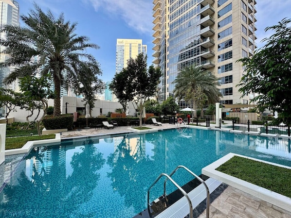 A swimming pool with lounge chairs and palm trees, surrounded by high-rise buildings.