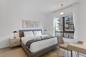 A modern hotel room with a bed, bedside tables, a desk, and a large window with a city view. - Exquisite and Capacious 1BR in South Ridge 3 (Dubai)