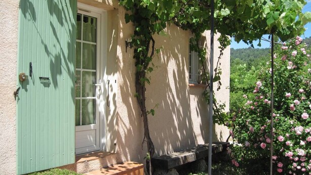 Un edificio rústico con una puerta verde, un banco de piedra y una pared cubierta de hiedra.
