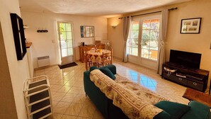 Una sala de estar con sofá, televisión, mesa de comedor y ventana con cortinas.