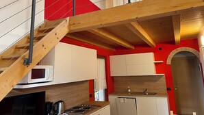 A kitchen with wooden beams, white cabinets, and a red accent wall. - App 5 Villa P. Ideal for 4 people with pool for a vacation of sports and relaxation (Malcesine)