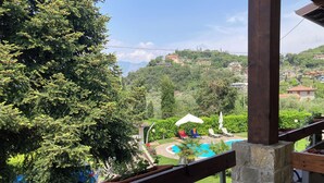 A balcony with a view of a swimming pool, lush greenery, and distant buildings. - App 5 Villa P. Ideal for 4 people with pool for a vacation of sports and relaxation (Malcesine)