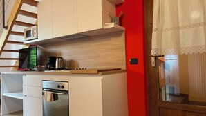 A compact kitchen with white cabinets, a built-in oven, and a red accent wall. - App 5 Villa P. Ideal for 4 people with pool for a vacation of sports and relaxation (Malcesine)