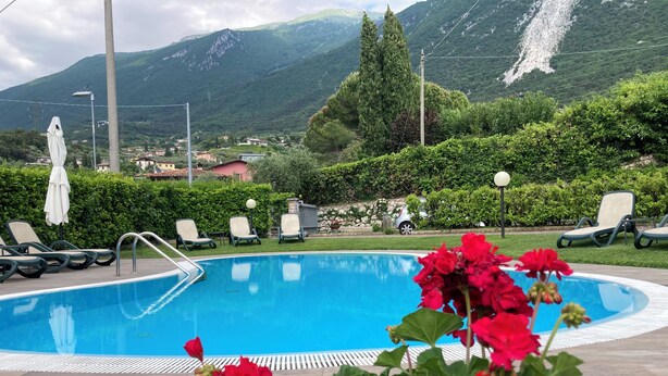A swimming pool with lounge chairs, surrounded by greenery and mountains in the background. - App 5 Villa P. Ideal for 4 people with pool for a vacation of sports and relaxation (Malcesine)