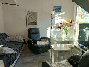 A living room with a sofa, a chair, a small table, a TV, a framed picture, and a vase with flowers.