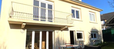 Une maison à deux étages avec un balcon, une porte-fenêtre coulissante et une terrasse équipée d’une table et de chaises.