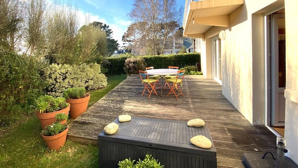 Una terraza de madera con una mesa y sillas, rodeada de macetas y un seto.