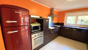 Una cocina compacta con un refrigerador rojo, un horno empotrado y un microondas.