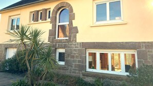 Una casa de dos pisos con fachada de piedra, ventanas grandes y un ventanal central arqueado.