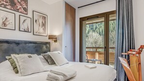 Ein Schlafzimmer mit einem großen Bett, einem hölzernen Kopfende, einem kleinen Tisch und Blick auf einen Balkon mit Holzgeländer.