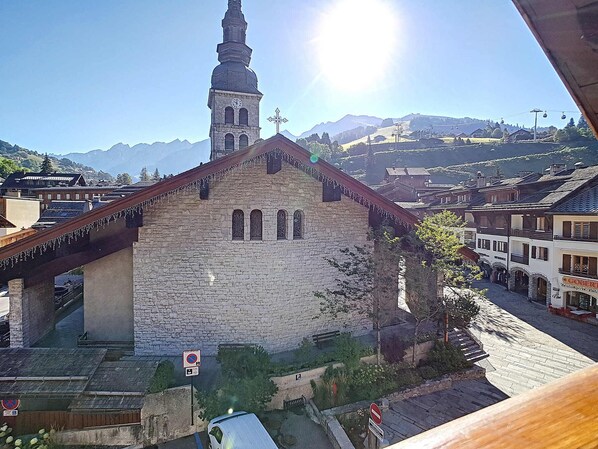A stone church with a bell tower, a pedestrian bridge, and a mountain backdrop. - La Clusaz Apartment 4 people with Wifi and pets allowed (La Clusaz)