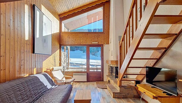 Un interno accogliente di una baita con arredamento in legno, un divano, una TV e un caminetto.
