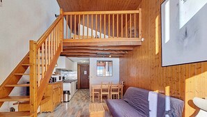 Una stanza in stile loft con una scala in legno, un divano, un tavolo da pranzo e un angolo cottura.