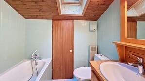 Un bagno con finestra sul tetto, soffitto in legno, vasca, water e lavandino.