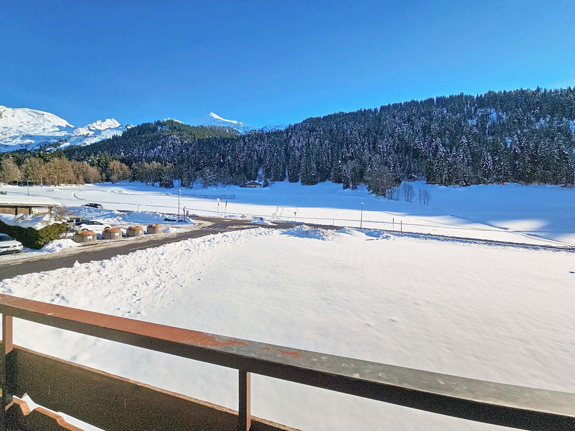 Un paisaje nevado con una carretera, una cerca y un edificio a lo lejos.