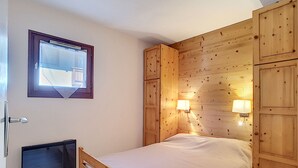Un dormitorio con estructura de cama de madera, una ventana con vistas y dos luces fijadas a la pared.
