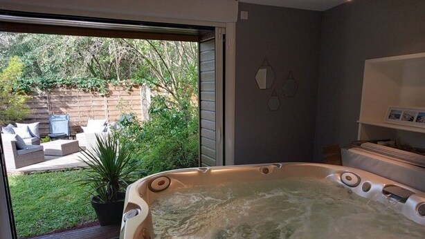 A spa room with a hot tub, a view of a backyard with outdoor furniture, and a wall-mounted light fixture. - Charming Cottage with Spa, Billiards, Garden and Ping-Pong (Vinon)
