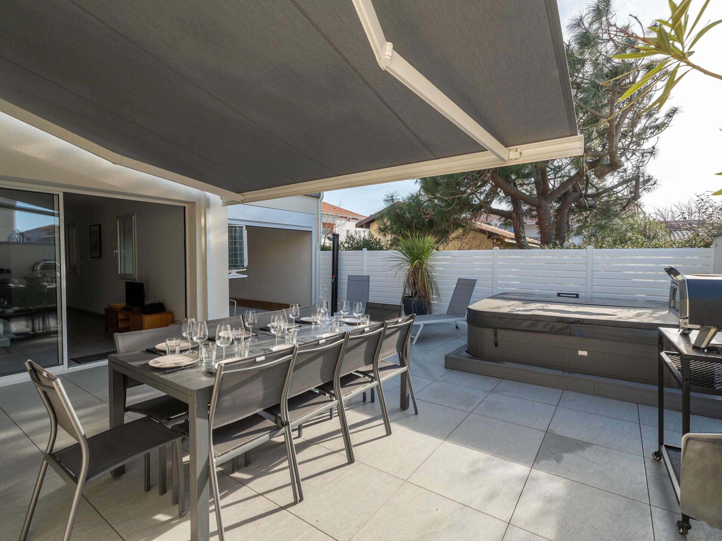 An outdoor patio with a table set for dining, a hot tub, and a grill area.