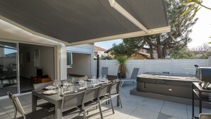 Une terrasse extérieure avec une table dressée pour les repas, un jacuzzi et un espace barbecue.