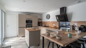 Une cuisine moderne dotée d’un îlot central, d’appareils électroménagers intégrés et d’une grande fenêtre offrant une vue dégagée.