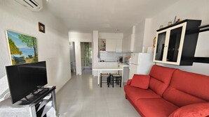 A living room with a red sofa, a TV, and a kitchen area with white cabinets. - Apartment with Wi-Fi & Parking, ideal for 4 in Roses (Roses)