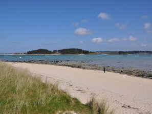 A beach with a sandy shore, a small island in the distance, and a person walking along the beach. - Cozy house 250m from Pors Gelen beach with garden and parking (Pleumeur-Bodou)