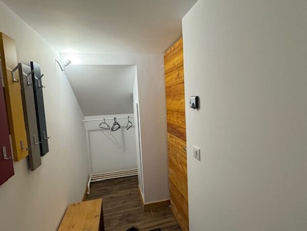 Un pasillo estrecho con suelo de madera, un radiador blanco y un perchero con ganchos.