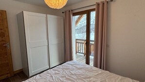 A bedroom with a bed, a wardrobe, and a view of a balcony.
