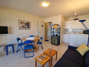 Un espacio habitable compacto con comedor, sofá, televisión, cocina y una pequeña mesa.